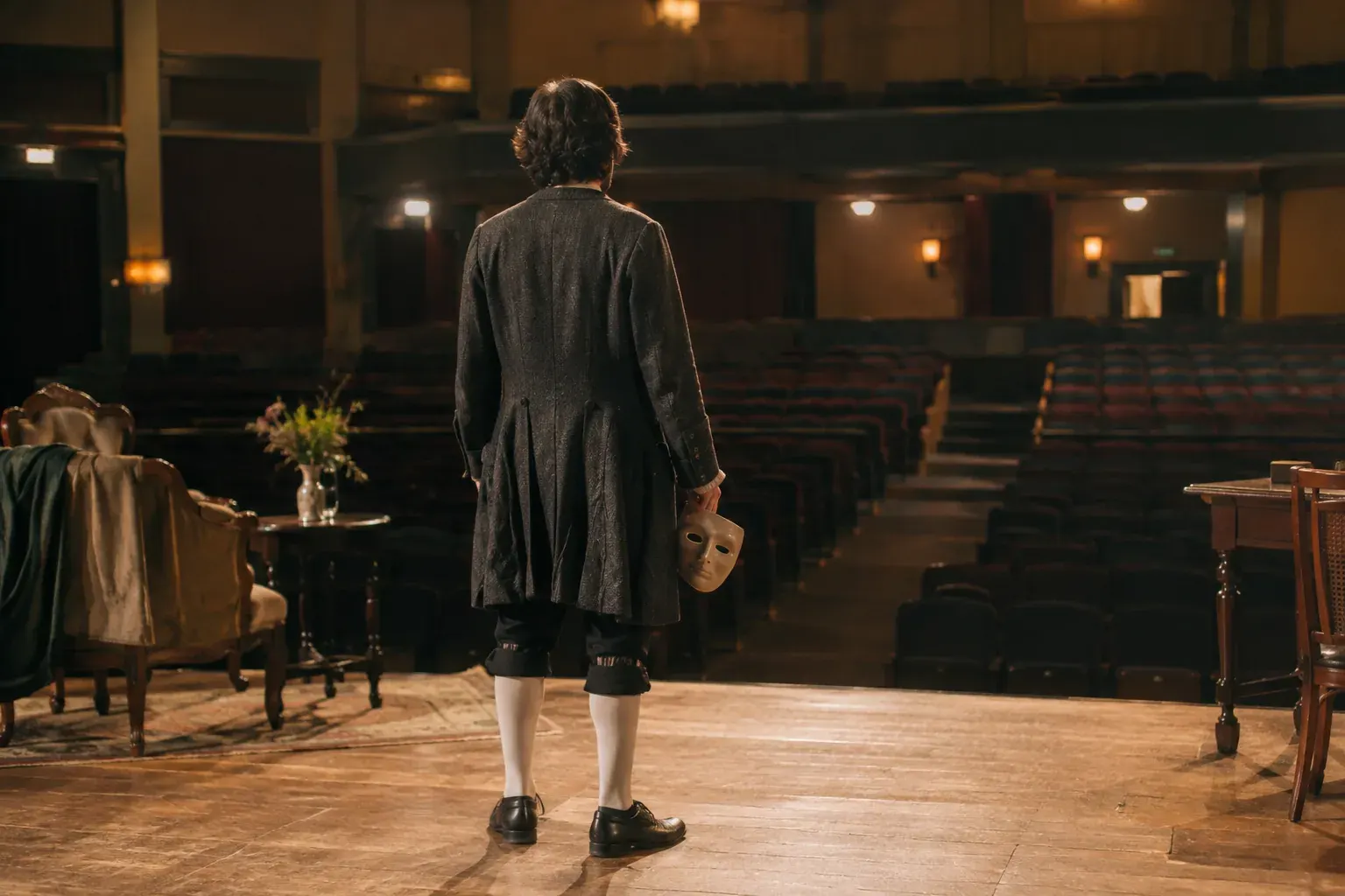 An actor in period-inspired costume rehearses on a small theater stage