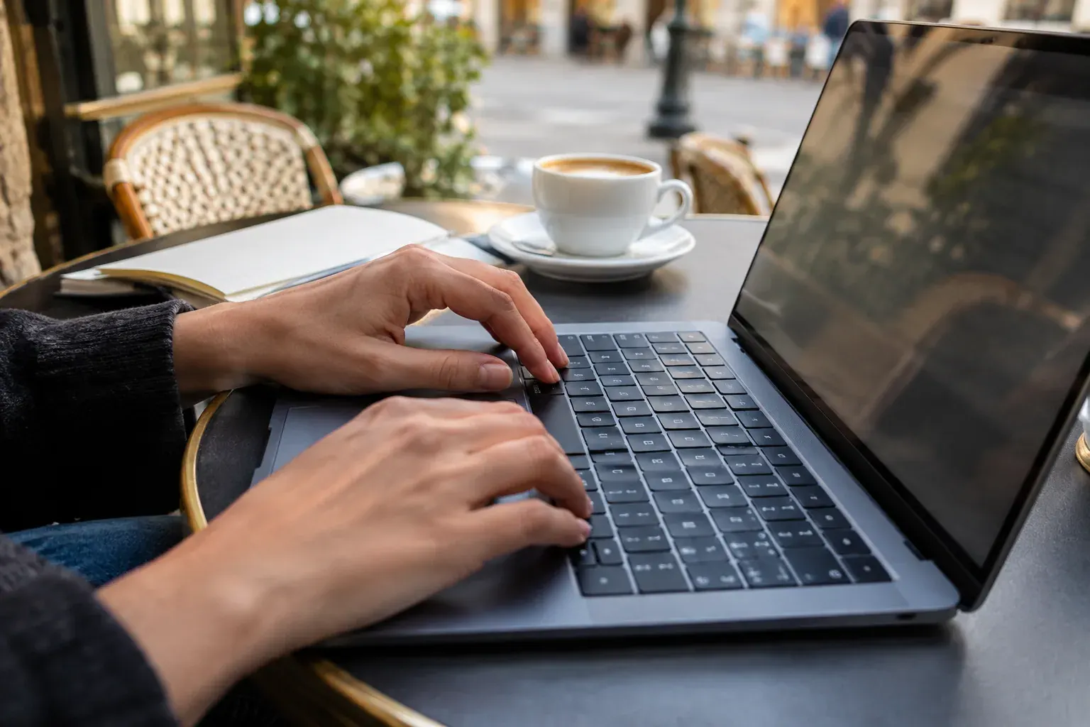Hands typing on a French AZERTY laptop keyboard at a cafe table.