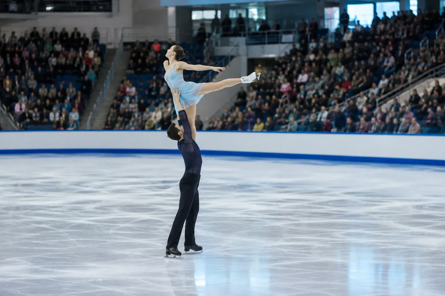 A figure skating pair performs a lift on an indoor rink during a competition.