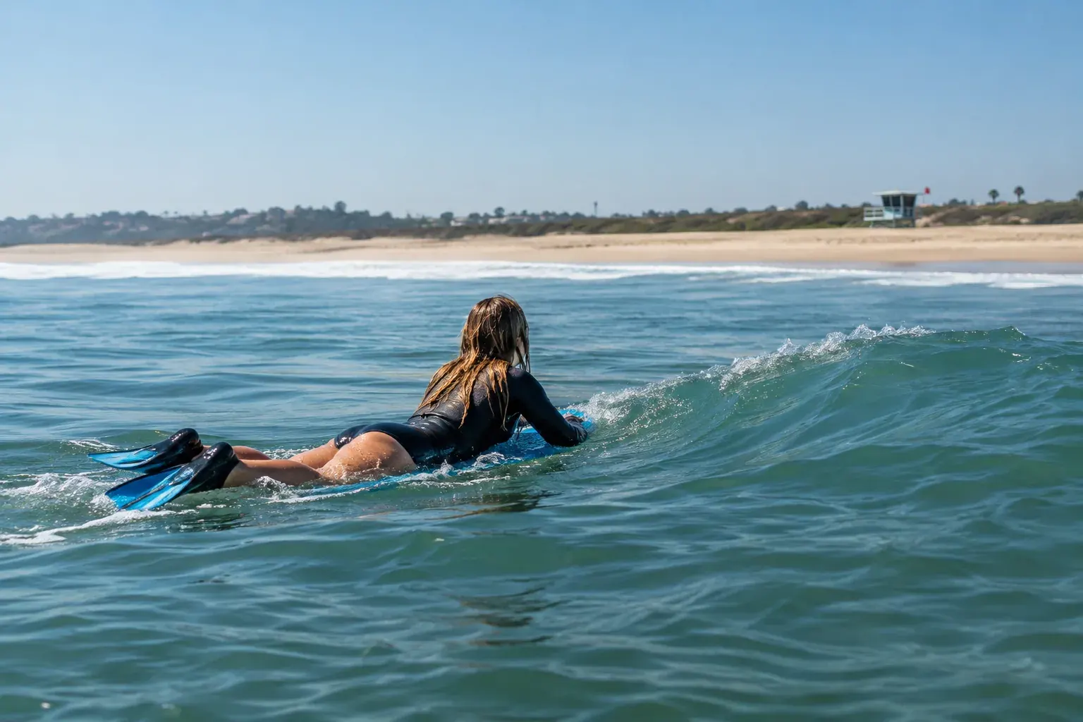 A beginner bodysurfer rides a small wave near a sandy beach.
